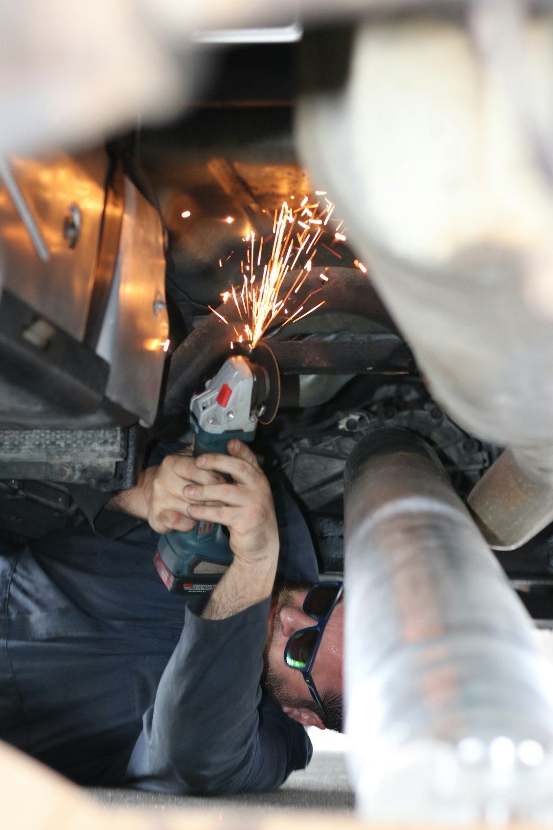 A mechanic working on replacing a drive shaft in a vehicle, set in an apartment complex in Colorado. The image shows a technician using specialized tools to remove and install the drive shaft, an essential component in the drivetrain system. Despite the unconventional location, the mechanic is focused on the task at hand, with various car parts and tools visible in the background. This scene is ideal for automotive repair guides, car maintenance tutorials, or DIY vehicle restoration projects.